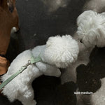White fluffy dog toy with a green leash on a dark background